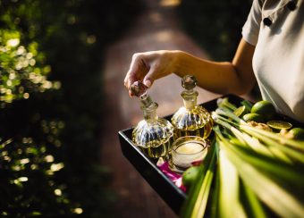 High angle close up of woman holding tray with glass bottles, candles and fruit.
