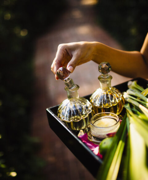 High angle close up of woman holding tray with glass bottles, candles and fruit.