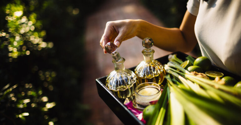 High angle close up of woman holding tray with glass bottles, candles and fruit.